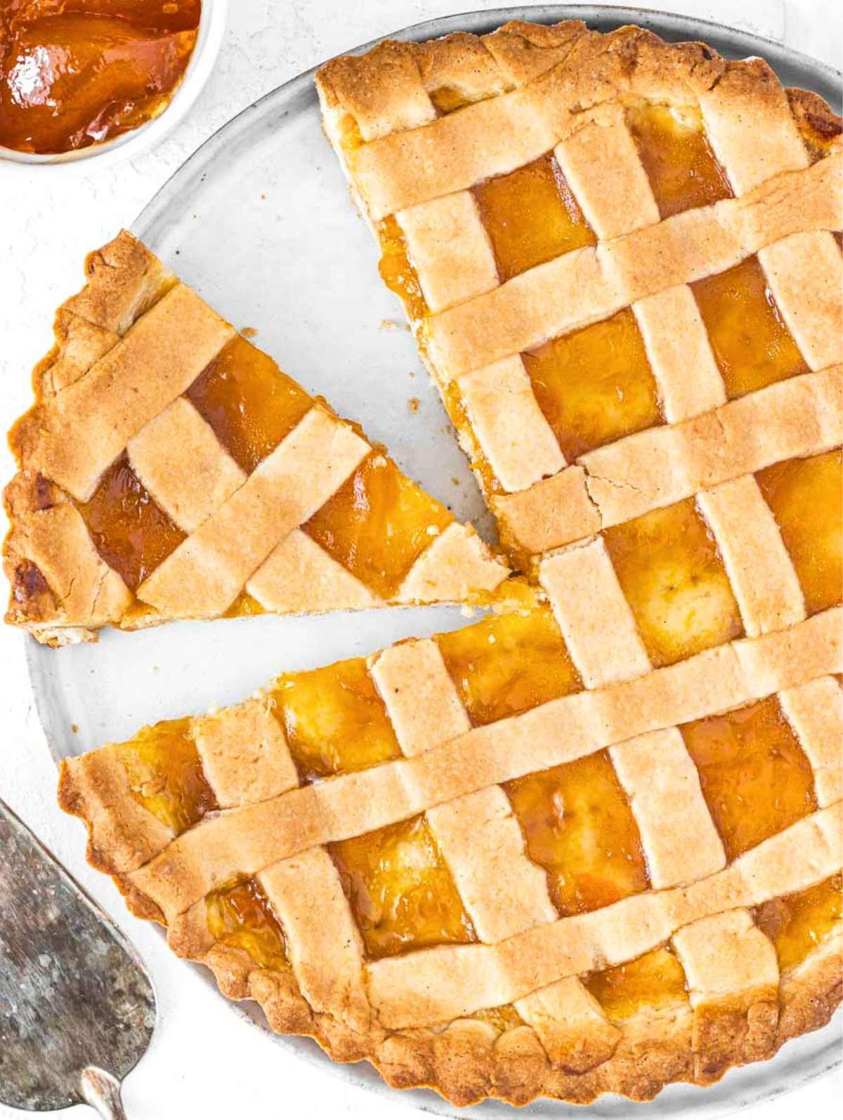 Italienische Crostata mit einem Stück und einer kleinen Schale Aprikosenmarmelade