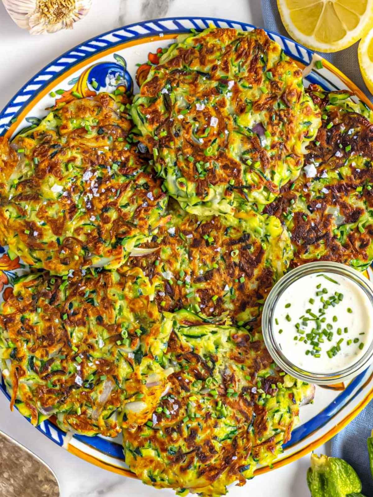 Zucchinipuffer auf einer Platte mit Zitrone serviert.