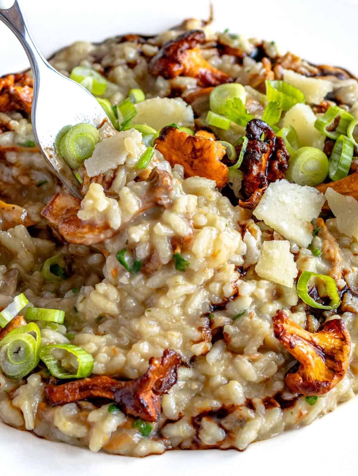 Pilzrisotto auf einem Teller mit einer Gabel und Lauchzwiebeln