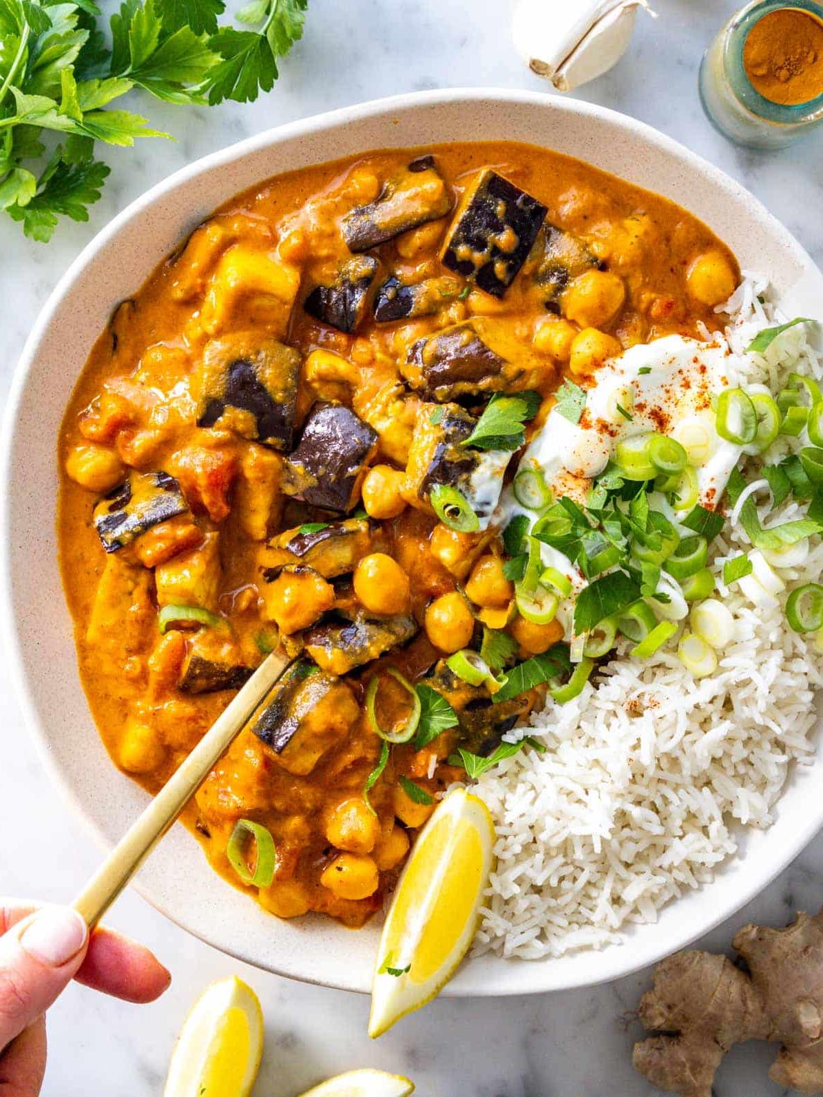 Auberginen-Curry mit Basmatireis und einer Hand, die einen Löffel hält.