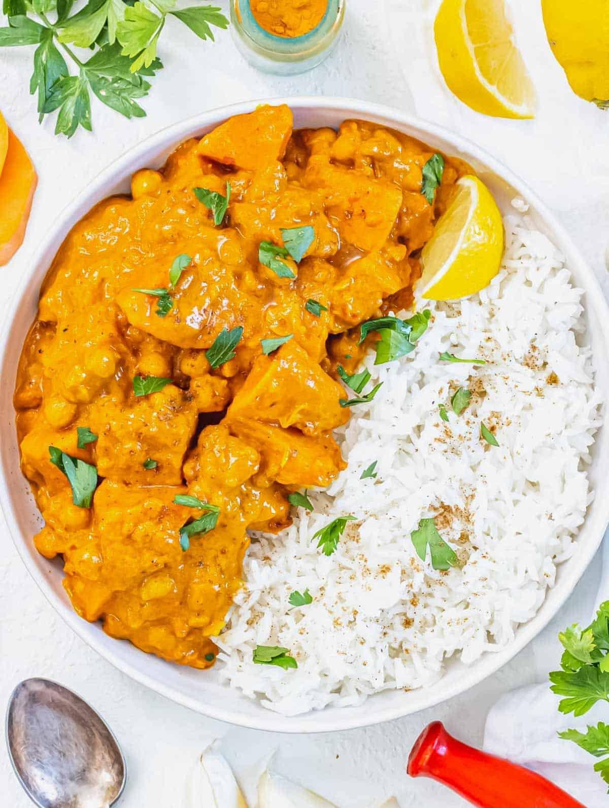 Süßkartoffel-Curry serviert mit Basmatireis, Zitrone und frischem Koriander. Ein köstliches, veganes One-Pot-Gericht.