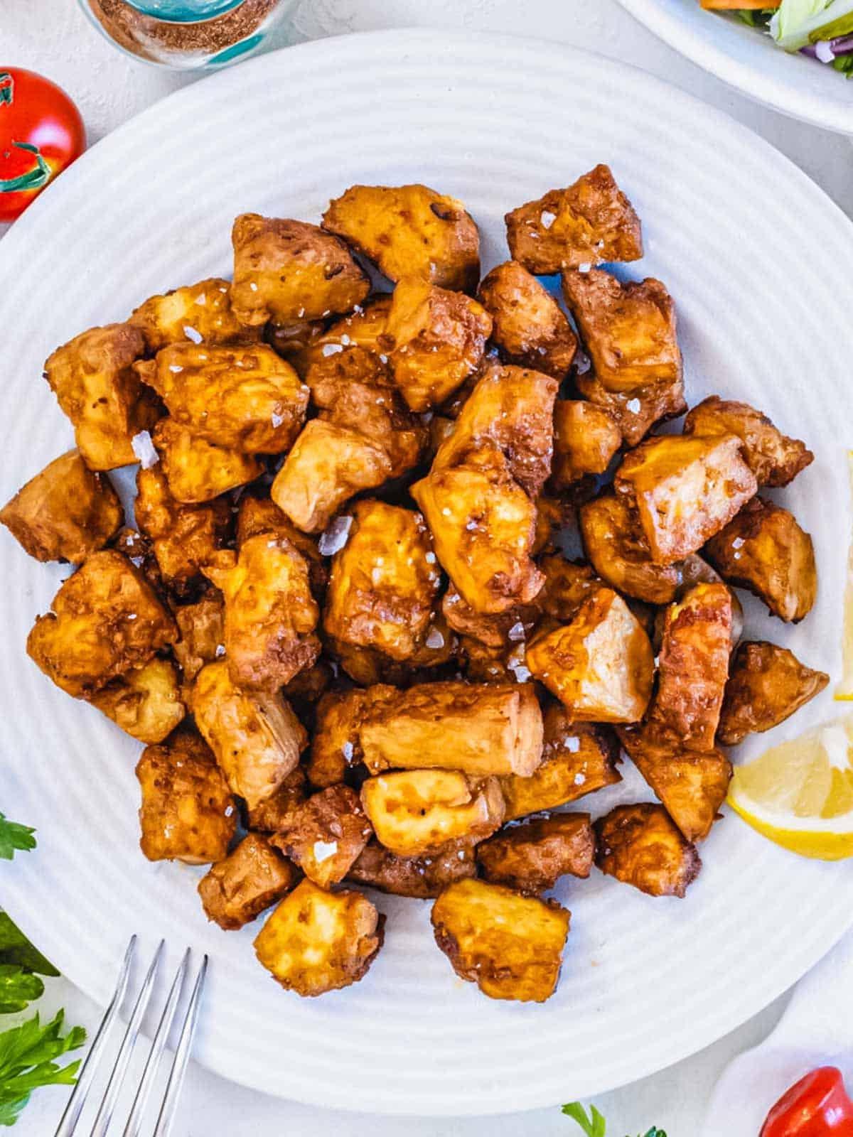 Tofu aus der Heißluftfritteuse. Ein golden-braun gebackenes Tofustück auf einem Holztisch.