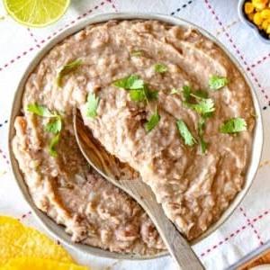 Refried Beans mit Koriander und einem Holzlöffel