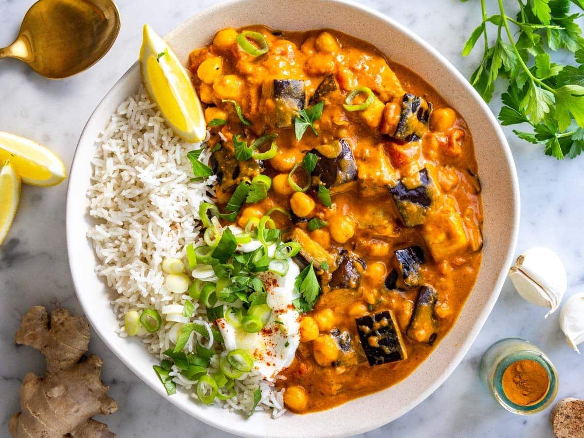 Auberginen-Curry serviert mit Basmatireis, Joghurt, Zitronensaft und Koriander.
