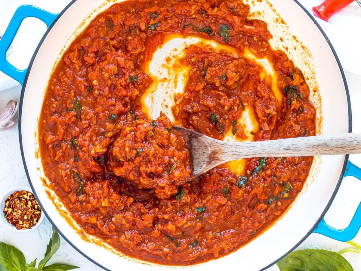 Marinara-Sauce mit Basilikum in einer Pfanne und einem Holzlöffel rührend.
