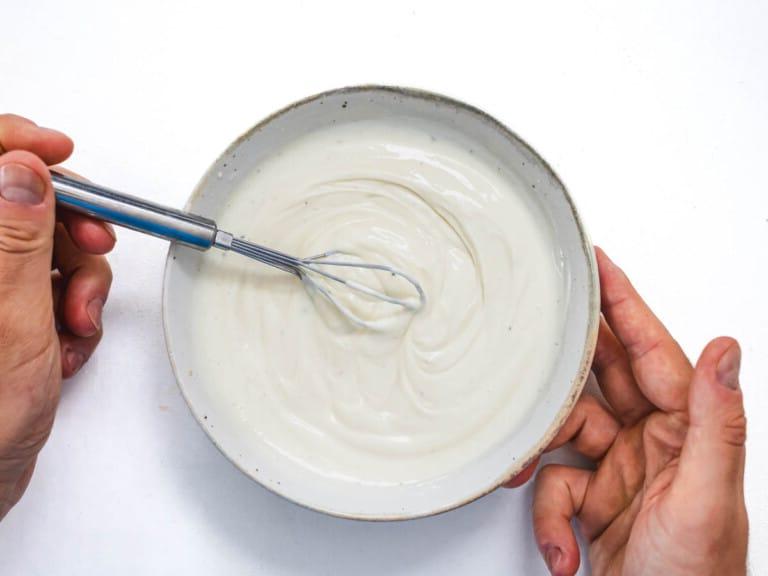 mayo yogurt dressing with hands and a whisk
