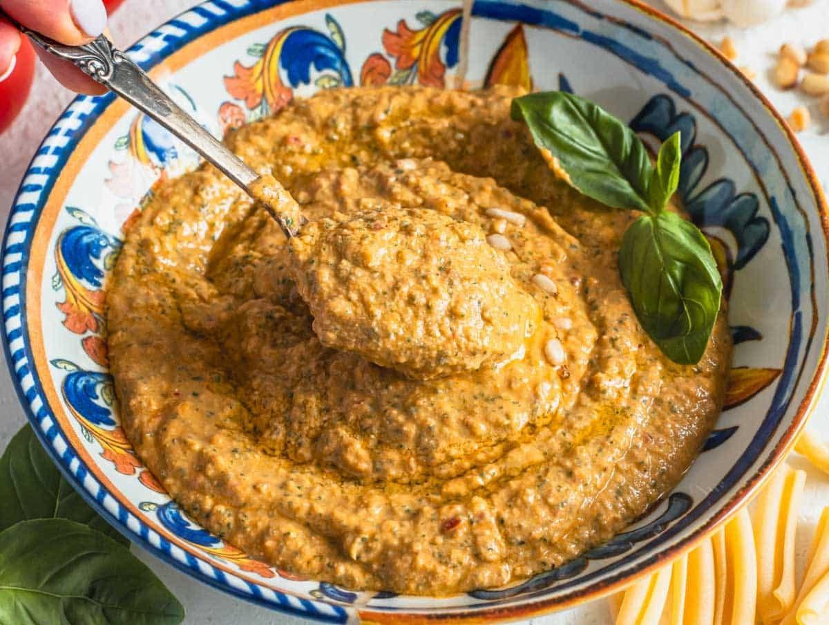 Rotes Tomatenpesto in einer blauen Schüssel mit einem silbernen Löffel
