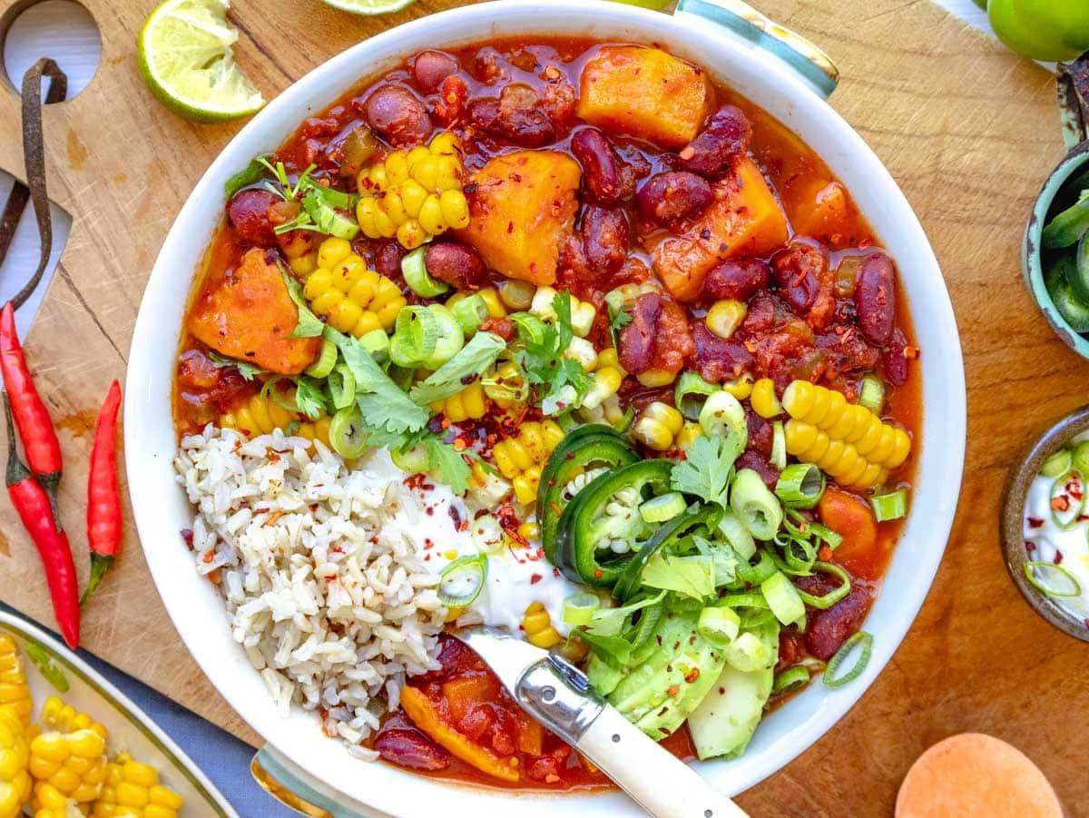 Süßkartoffel-Chili in einer Schüssel auf Reis und garniert mit Jalapeños, Koriander, Limette, Sauerrahm, Avocado und Mais.