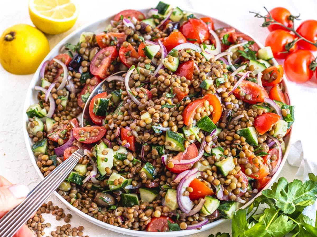 25 Vegane Salate 14 Linsensalat auf einem großen weißen Teller mit einer Hand, die einen silbernen Löffel hält