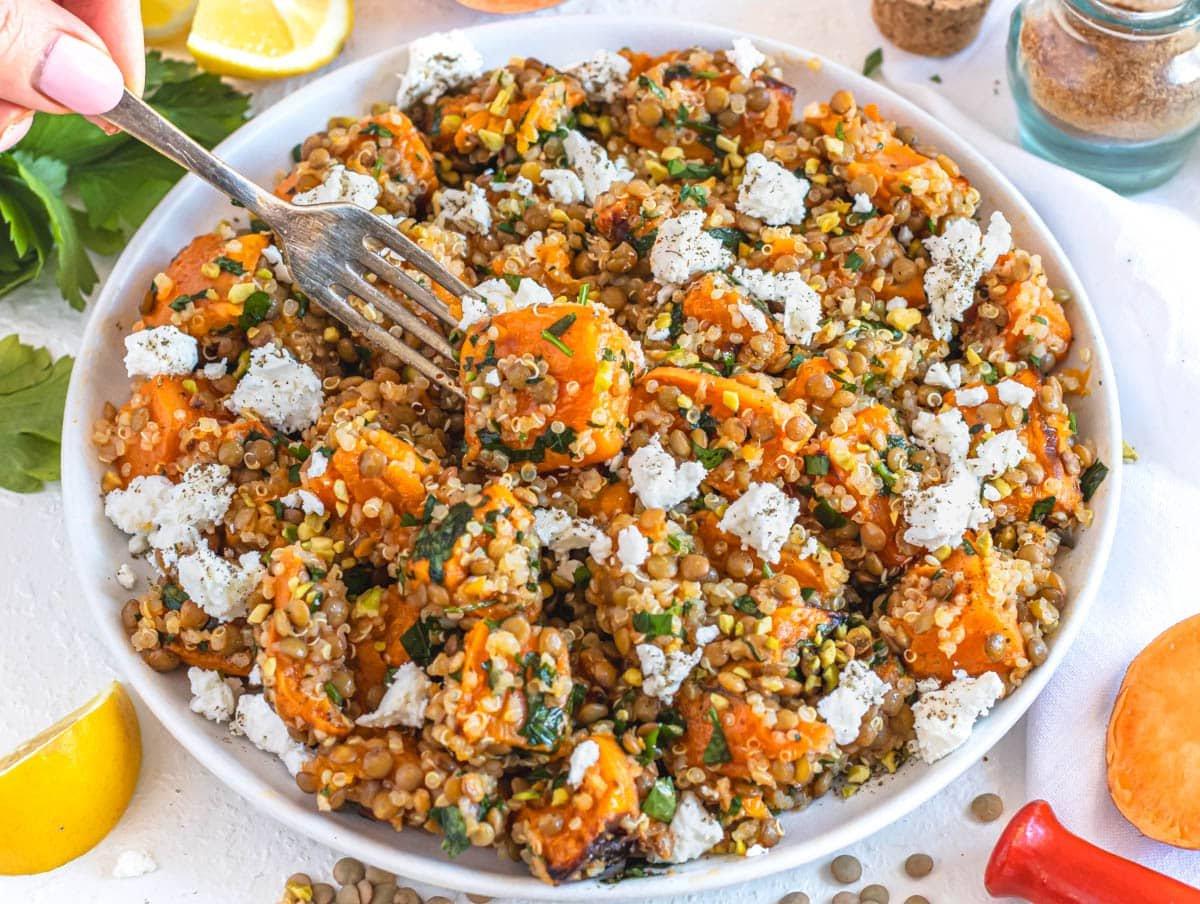 Linsen-Quinoa-Salat mit Feta und einer Hand, die eine Gabel hält
