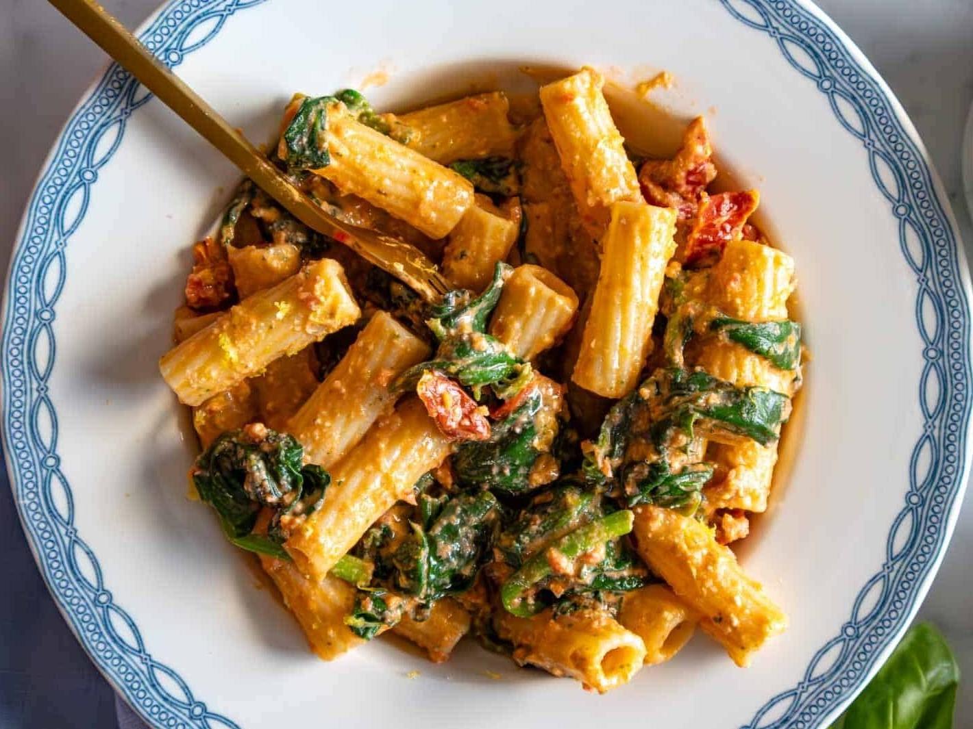 Getrocknete Tomaten Pasta mit Spinat auf einem blauen Teller.