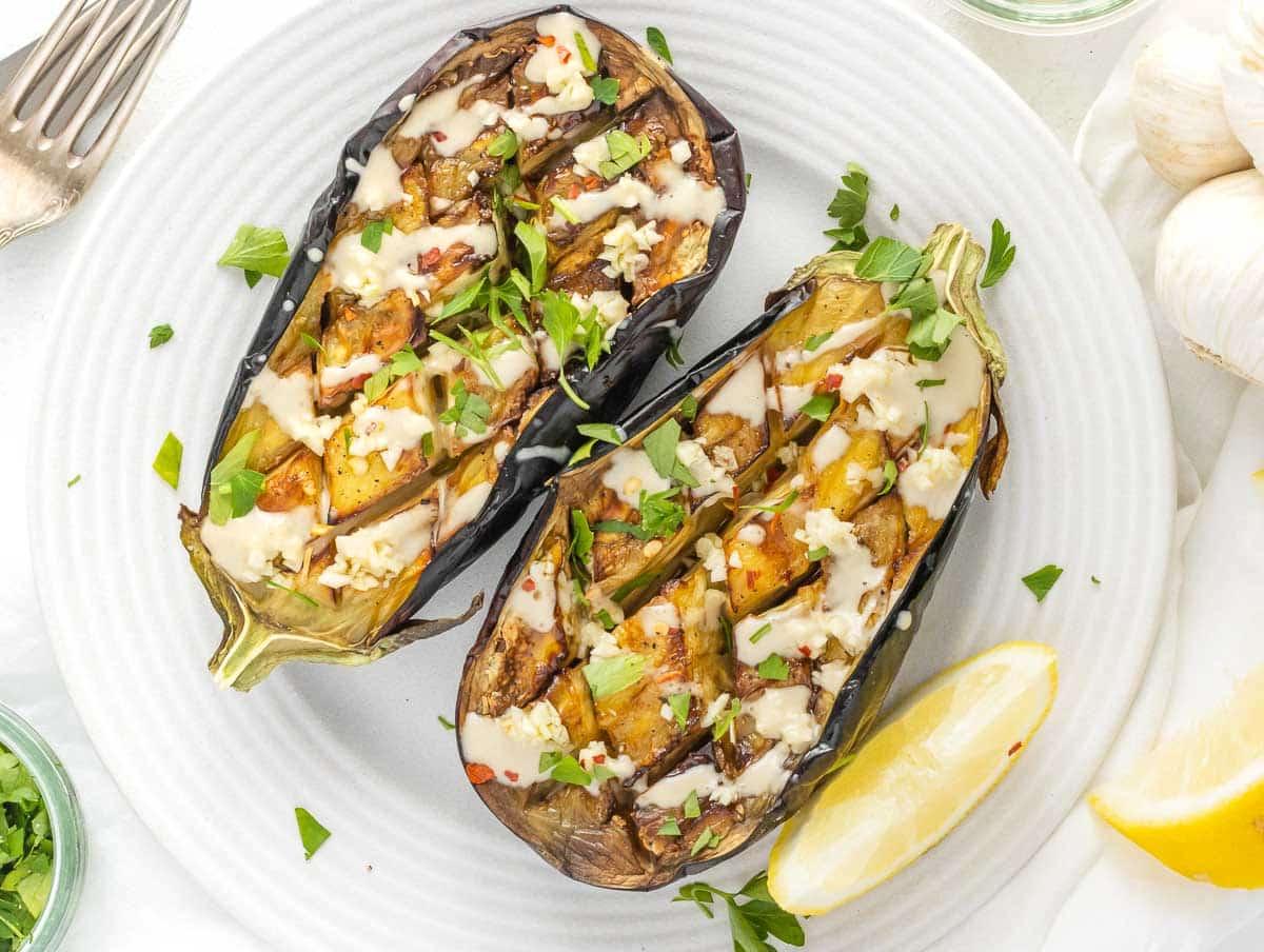 Heißluftfrittierte Auberginenboote mit Tahini-Soße, gehacktem Knoblauch und Petersilie