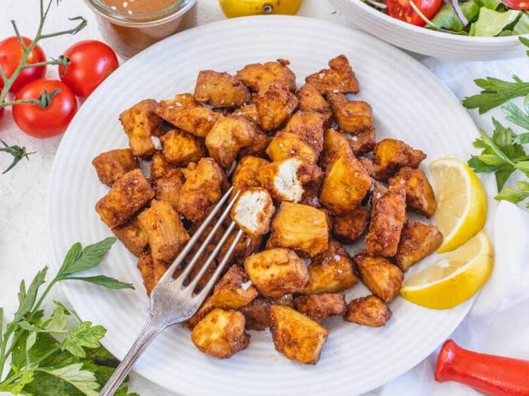 Tofu aus der Heißluftfritteuse auf einem Teller mit Zitronenspalten.