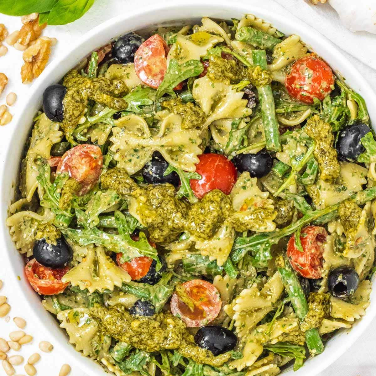Pesto-Nudelsalat in einer Schüssel mit Kirschtomaten und Oliven.