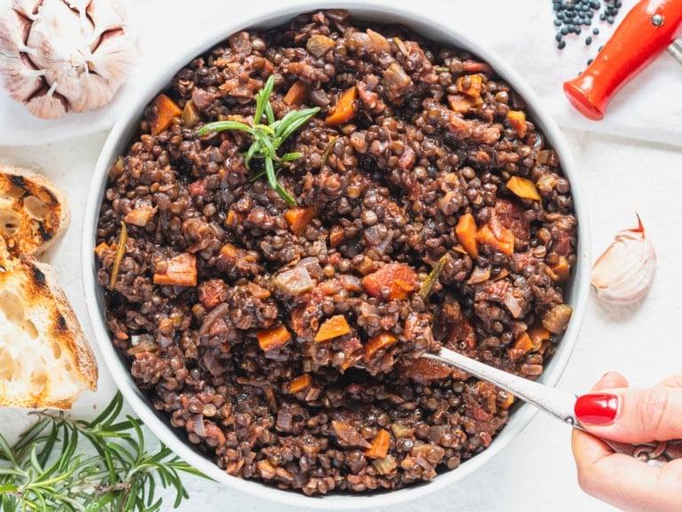 Schwarze Linsen mit einem Löffel und Hand mit rotem Nagel