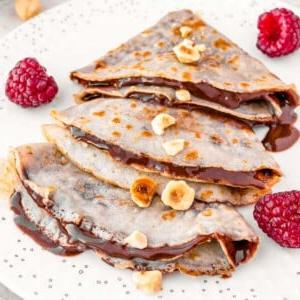 Vegane Crêpes auf einem weißen Teller mit Haselnüssen und Beeren