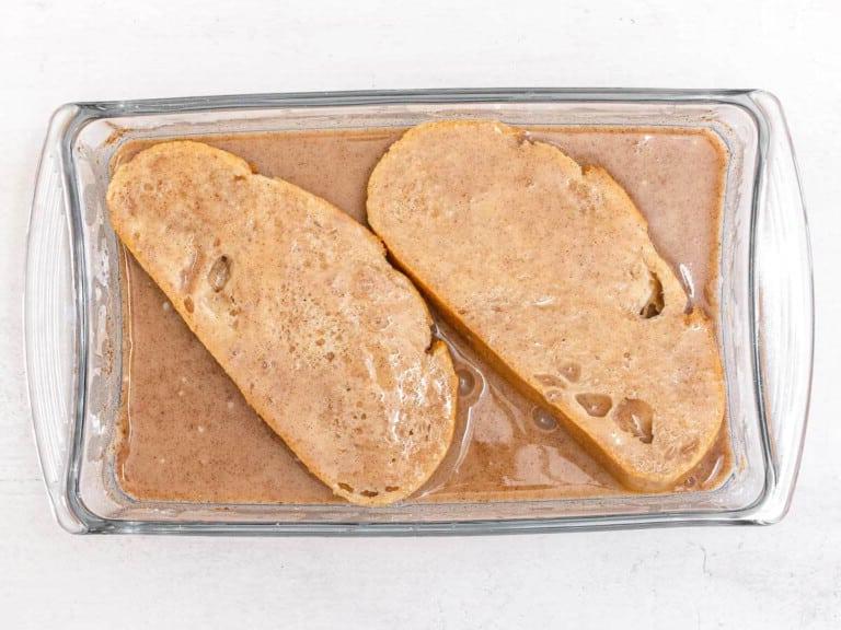 two slices of bread soaked in a cinnamon batter in a casserole