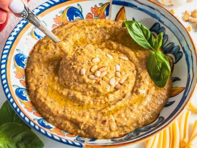 Rotes Tomatenpesto mit Pinienkernen und Hand, die einen Löffel hält