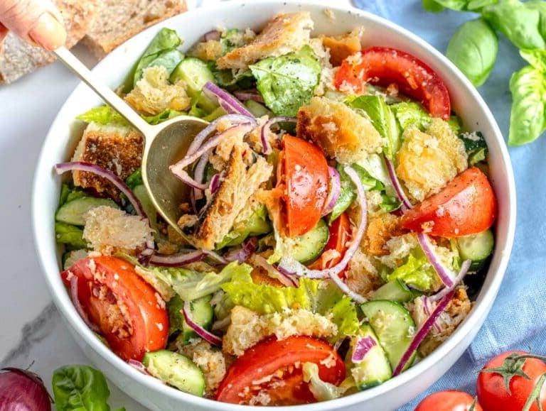 Panzanella Salat mit einer Hand, die einen goldenen Löffel hält
