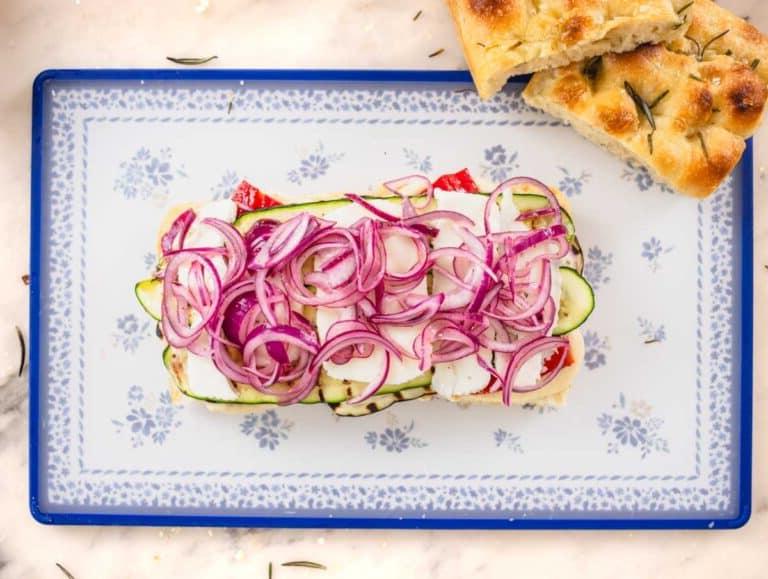 Focaccia Sandwich mit Gemüse und eingelegten roten Zwiebeln auf einem Schneidebrett