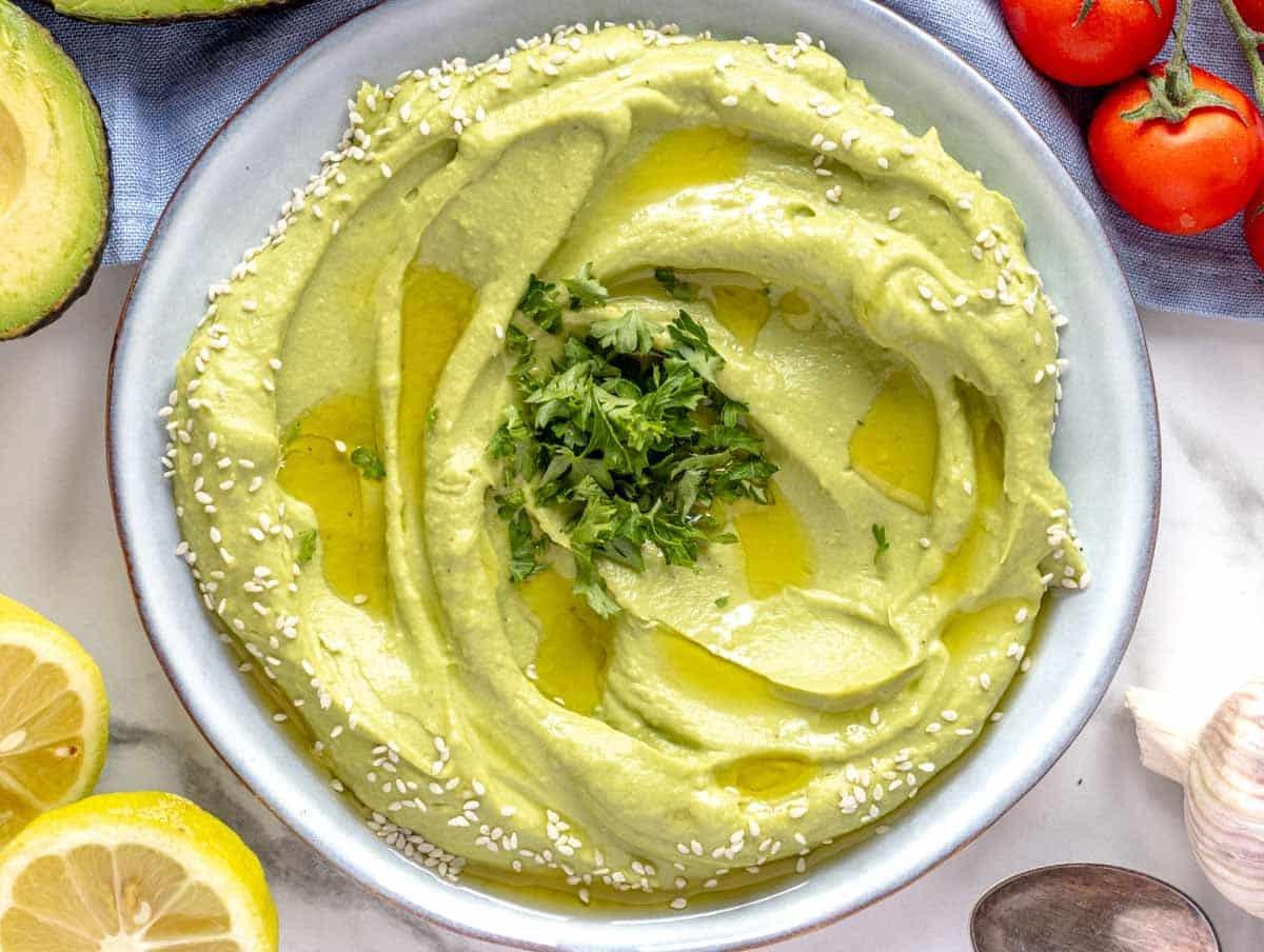 Cremiger Avocado-Aufstrich auf einem blauen Teller mit Zitrone daneben