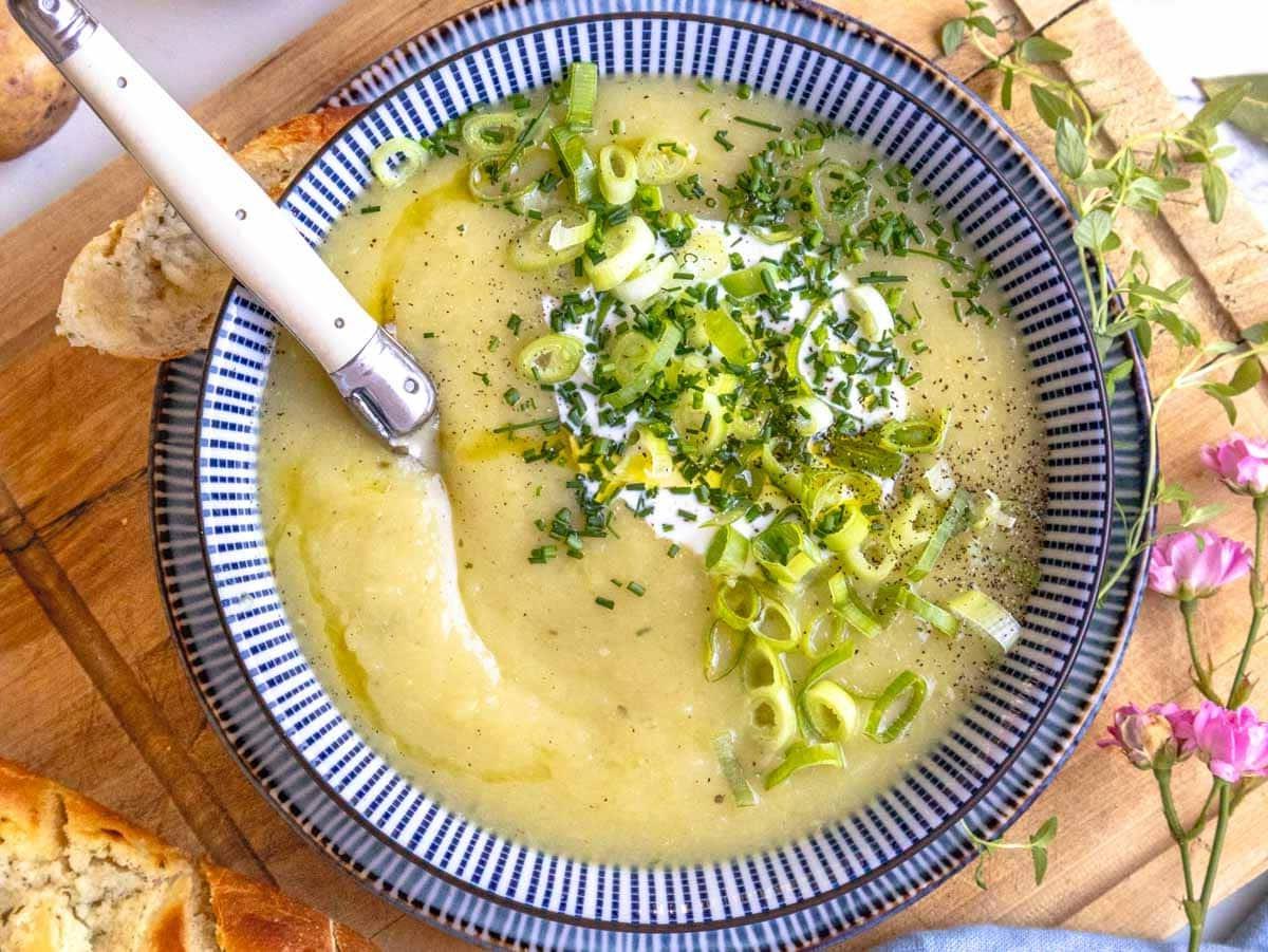 Kartoffel-Lauch-Suppe mit einem weißen Löffel und Knoblauchbrot als Beilage