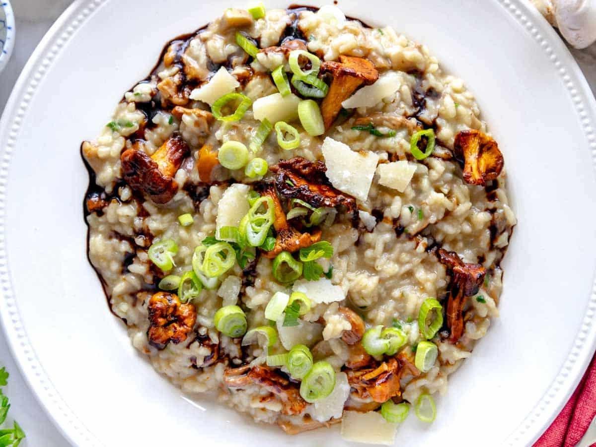 Pilzrisotto garniert mit gehobeltem Parmesan, Lauchzwiebeln und Balsamico-Glasur