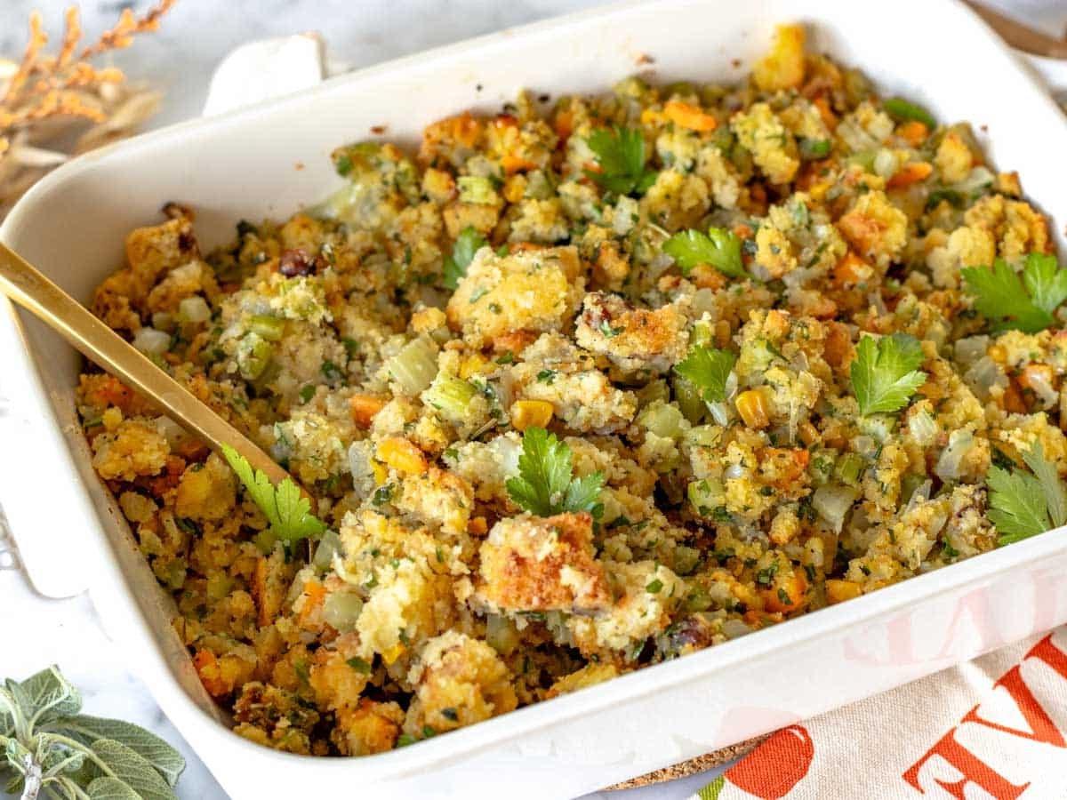 Cornbread Stuffing in einer weißen Auflaufform mit einem goldenen Löffel