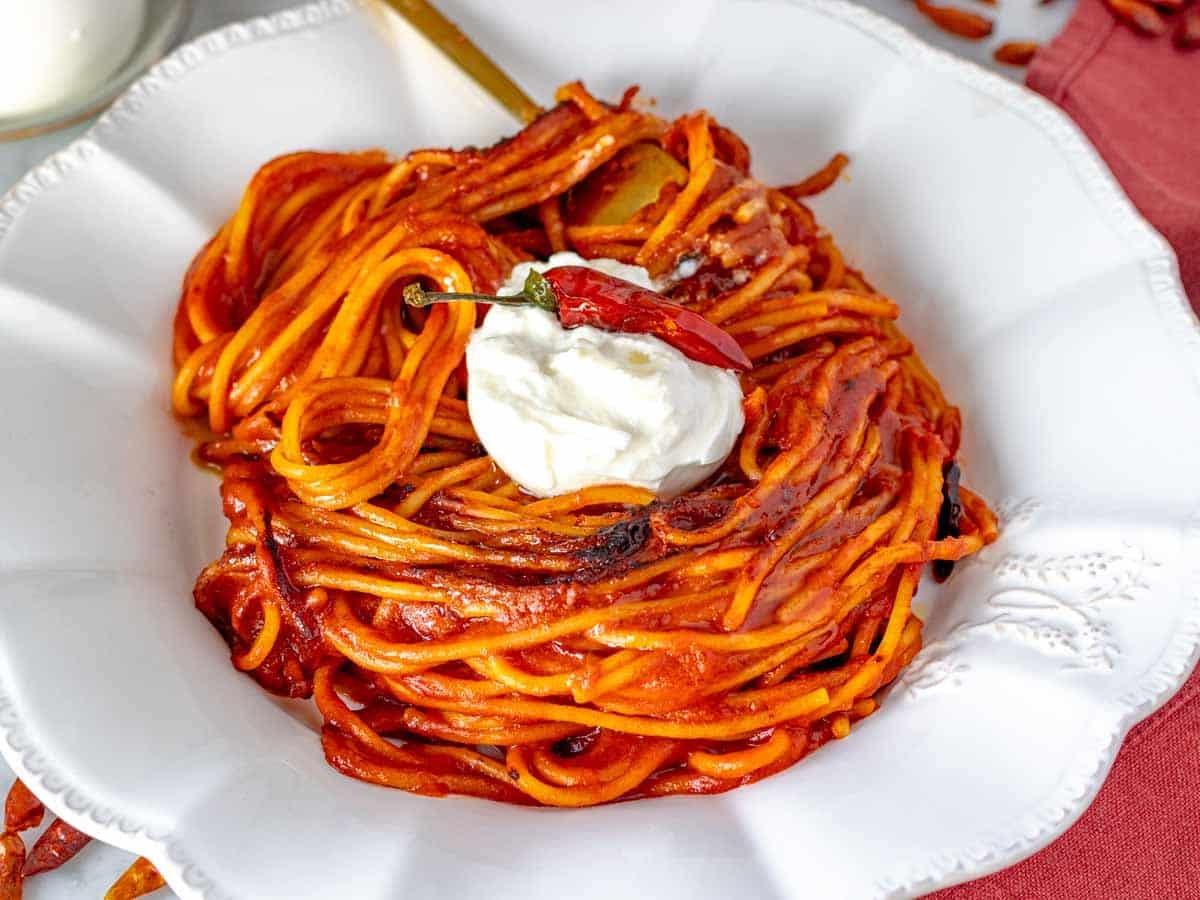 Assassin's Spaghetti auf einem weißen Teller mit Chili und einer goldenen Gabel.