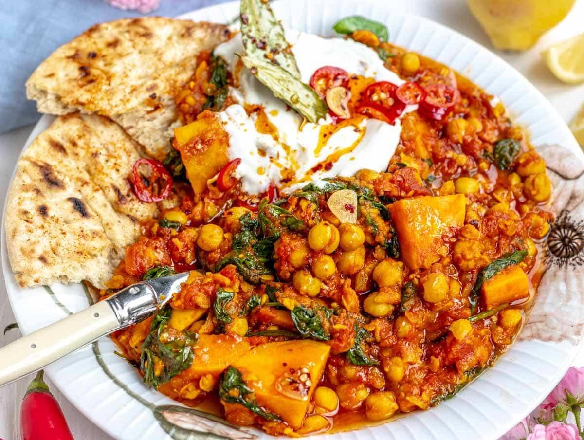 Kichererbseneintopf, serviert auf einem Teller mit Fladenbrot, Joghurt und Chili. Ein gesundes veganes Hauptgericht.
