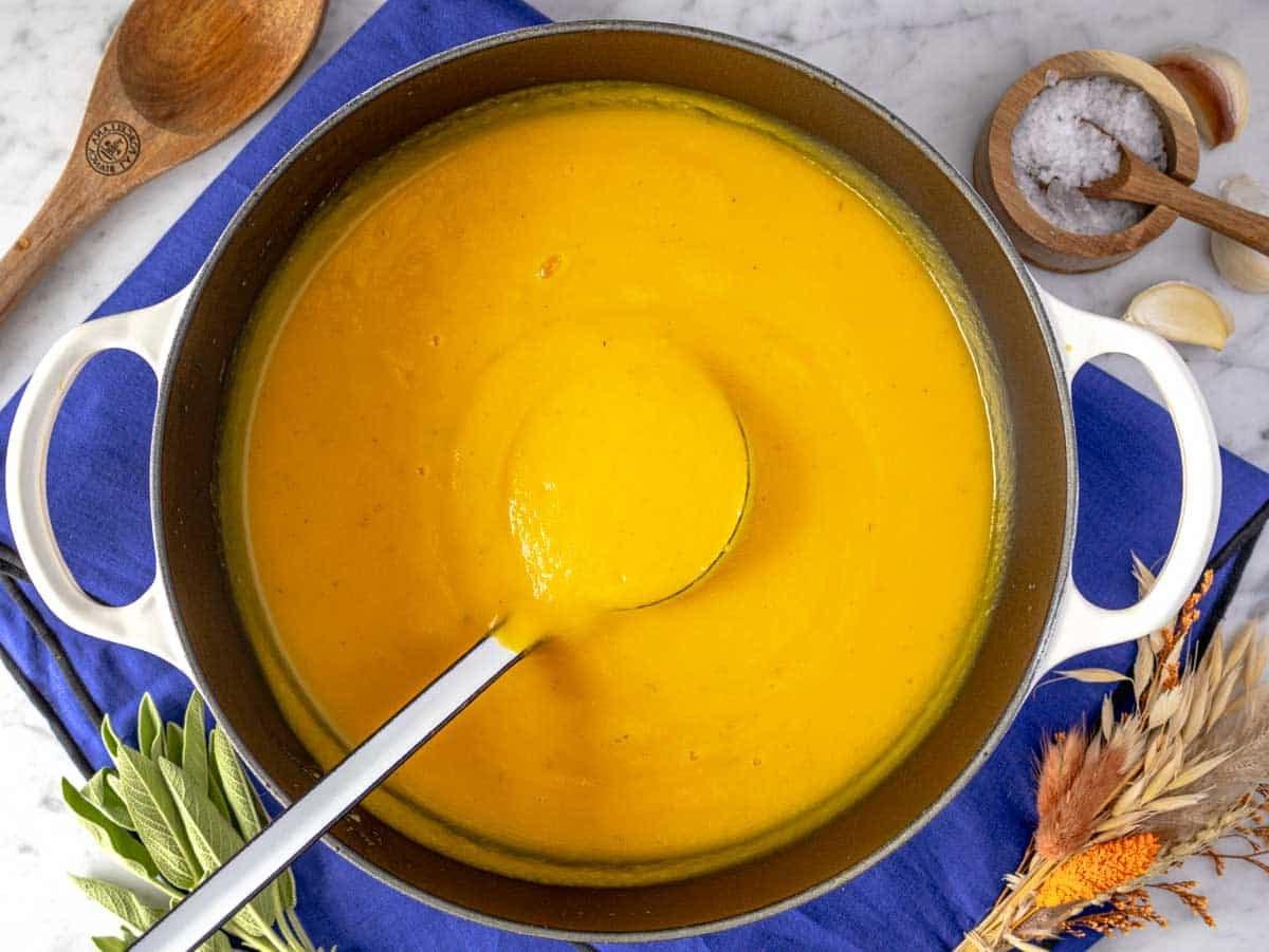 Easy butternut squash soup in a large pot with a ladle.