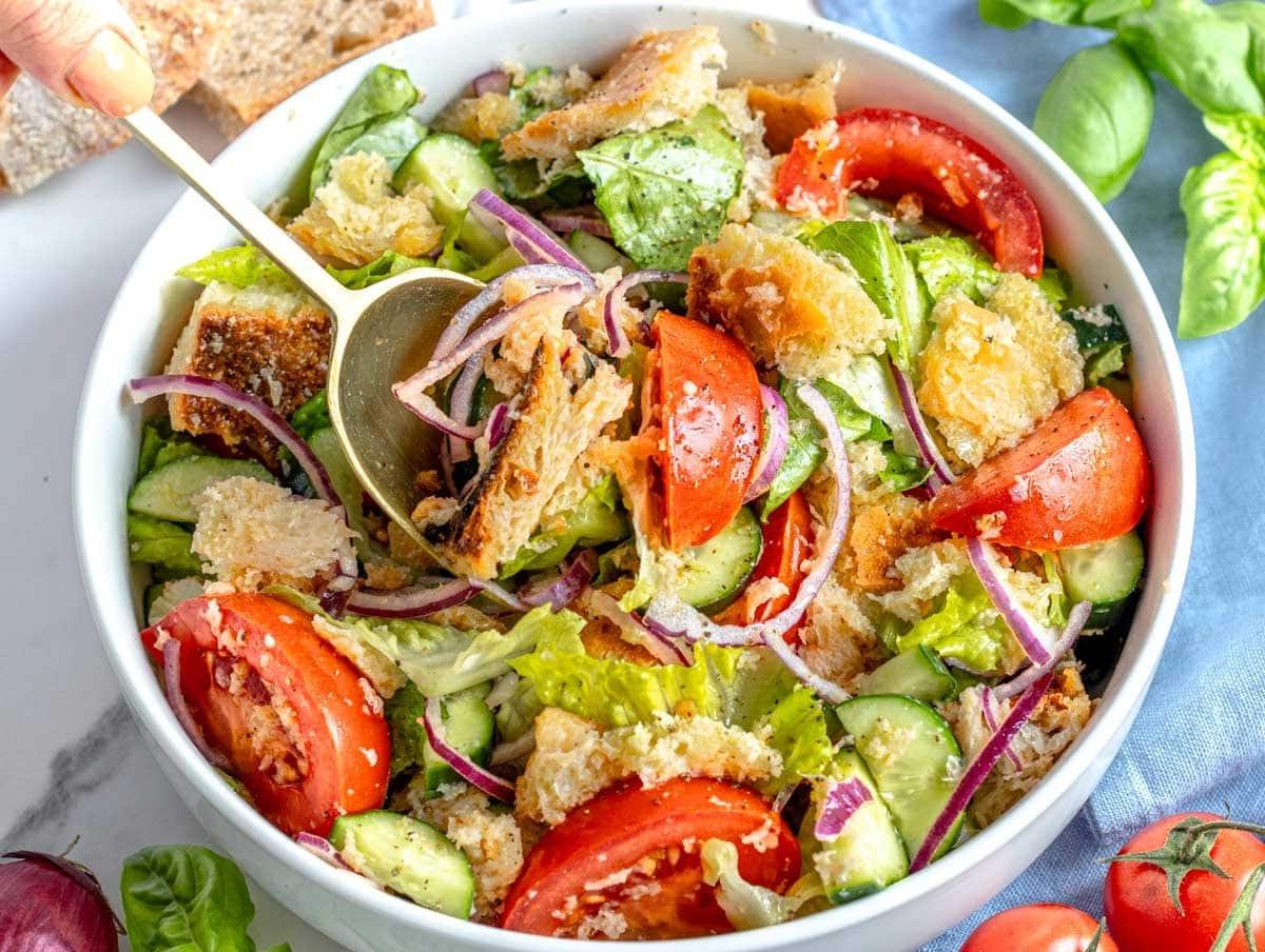 Panzanella Salat mit einer Hand, die einen goldenen Löffel hält