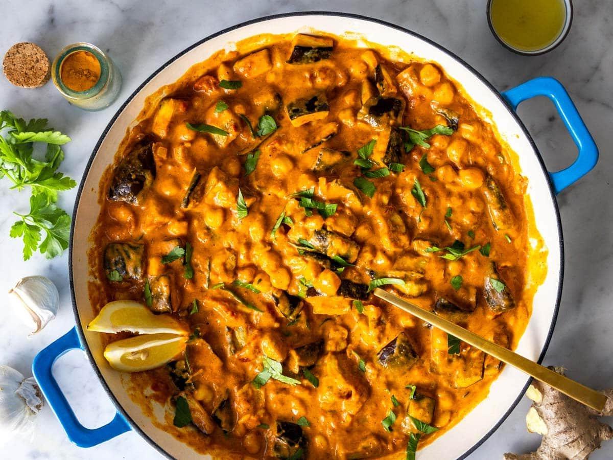 Auberginen-Curry in einer blauen Pfanne mit einem goldenen Löffel und Zitrone.