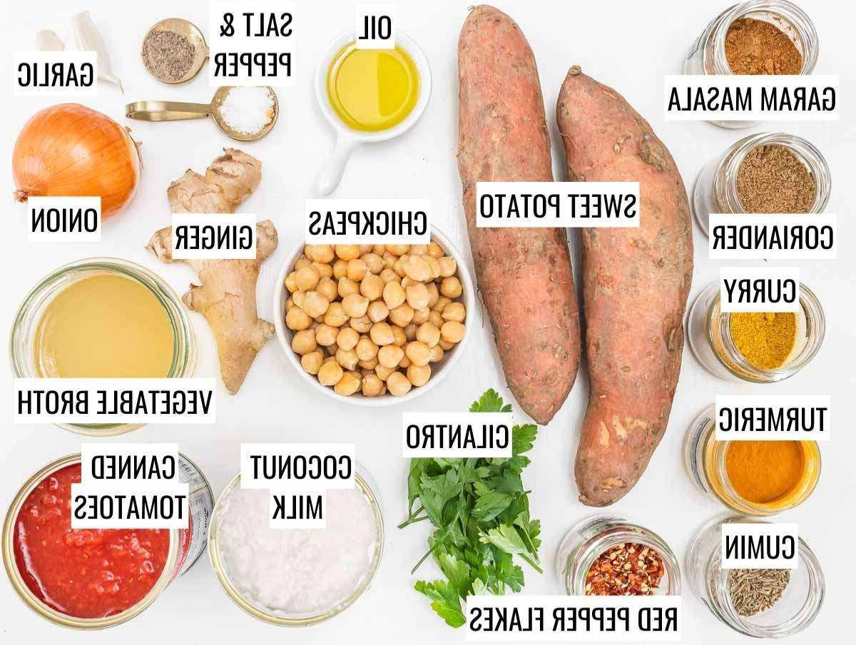 Zutaten für Süßkartoffel-Curry auf einem Holztisch, darunter Süßkartoffeln, Kichererbsen, Zwiebeln, Knoblauch und Gewürze.