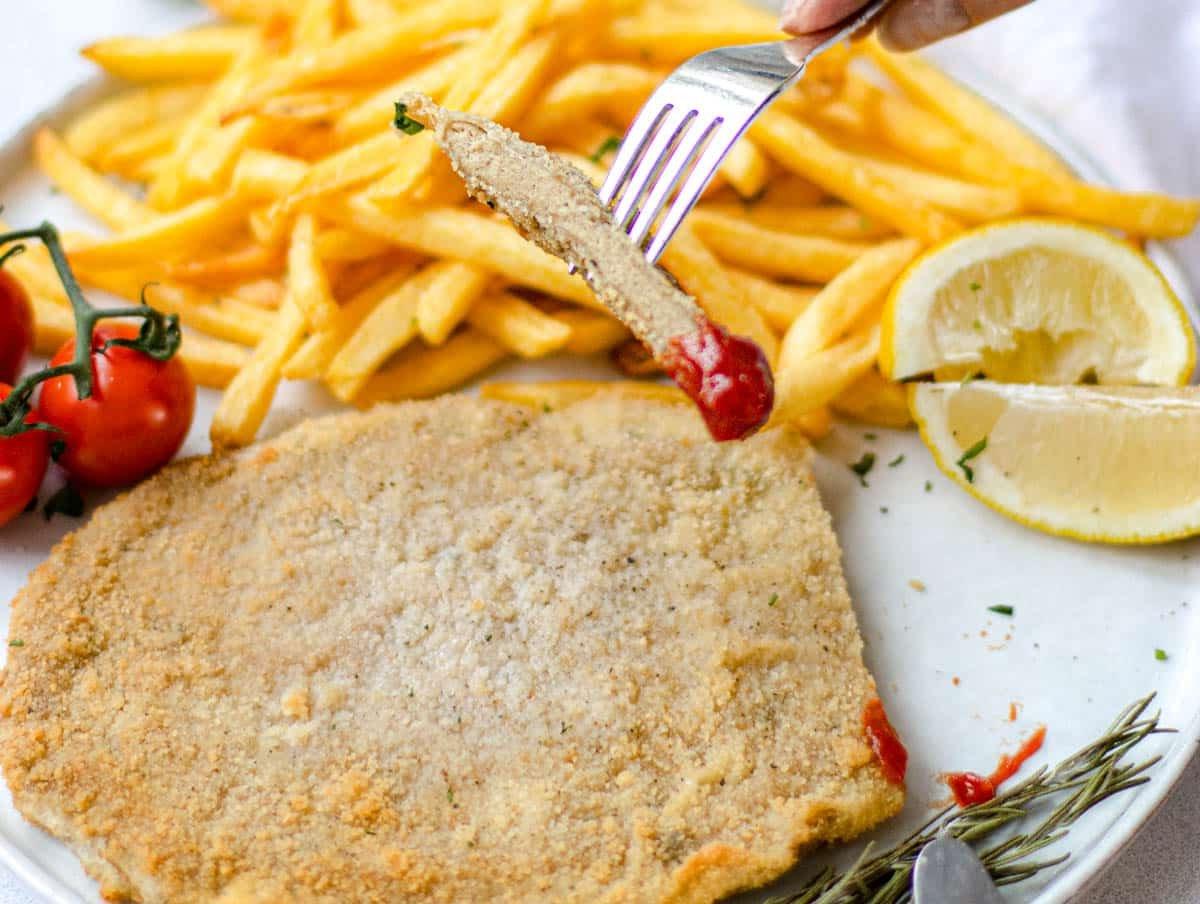 Veganes Schnitzel mit Ketchup und frischem Zitronensaft mit einer Hand, die eine Gabel hält