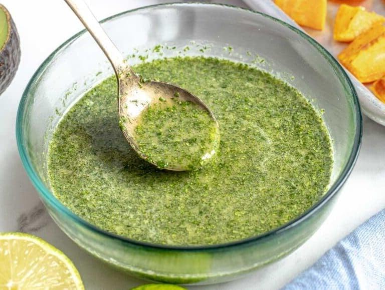 Cilantro lime dressing in a glass bowl with sweet potatoes and lime on the side