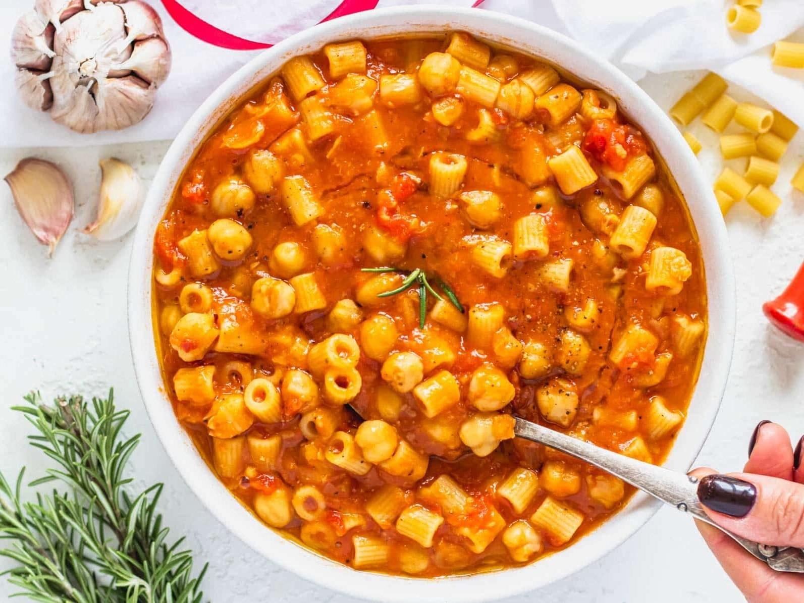 Pasta e Ceci in einer Schüssel mit einer Hand, die einen Löffel hält.