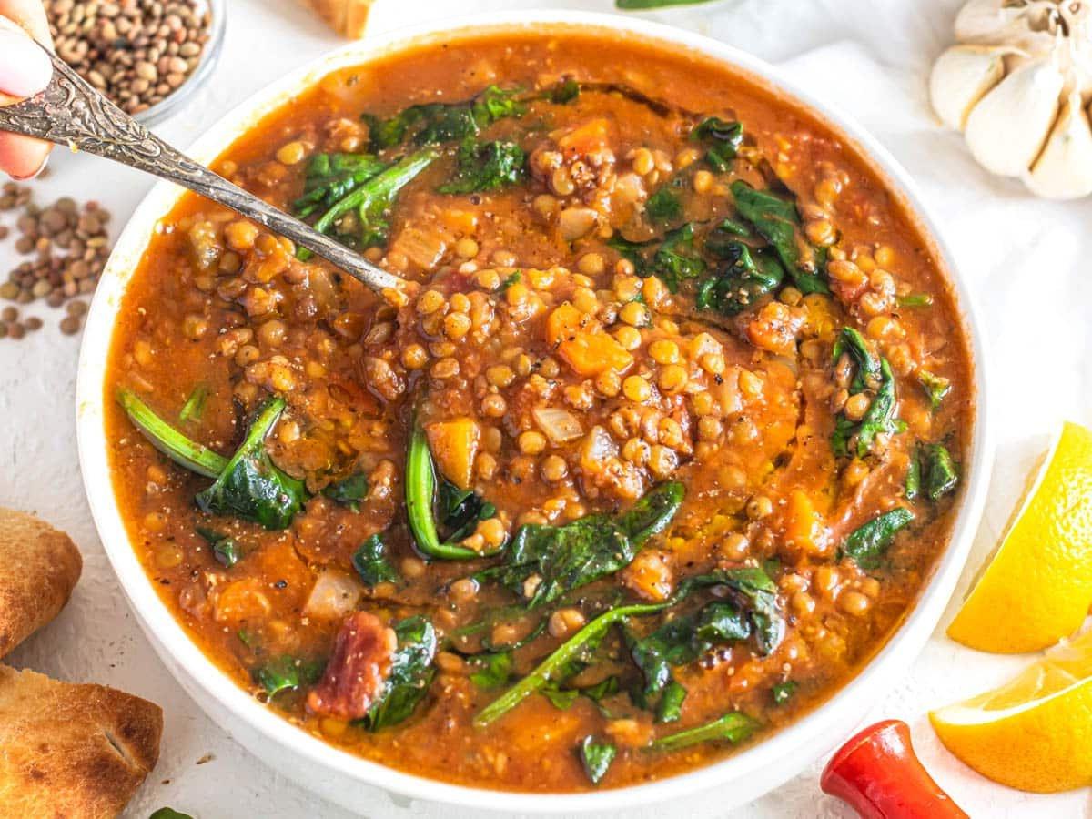 Einfache Linsen-Gemüse-Suppe mit einem silbernen Löffel in der Schüssel und Brot daneben