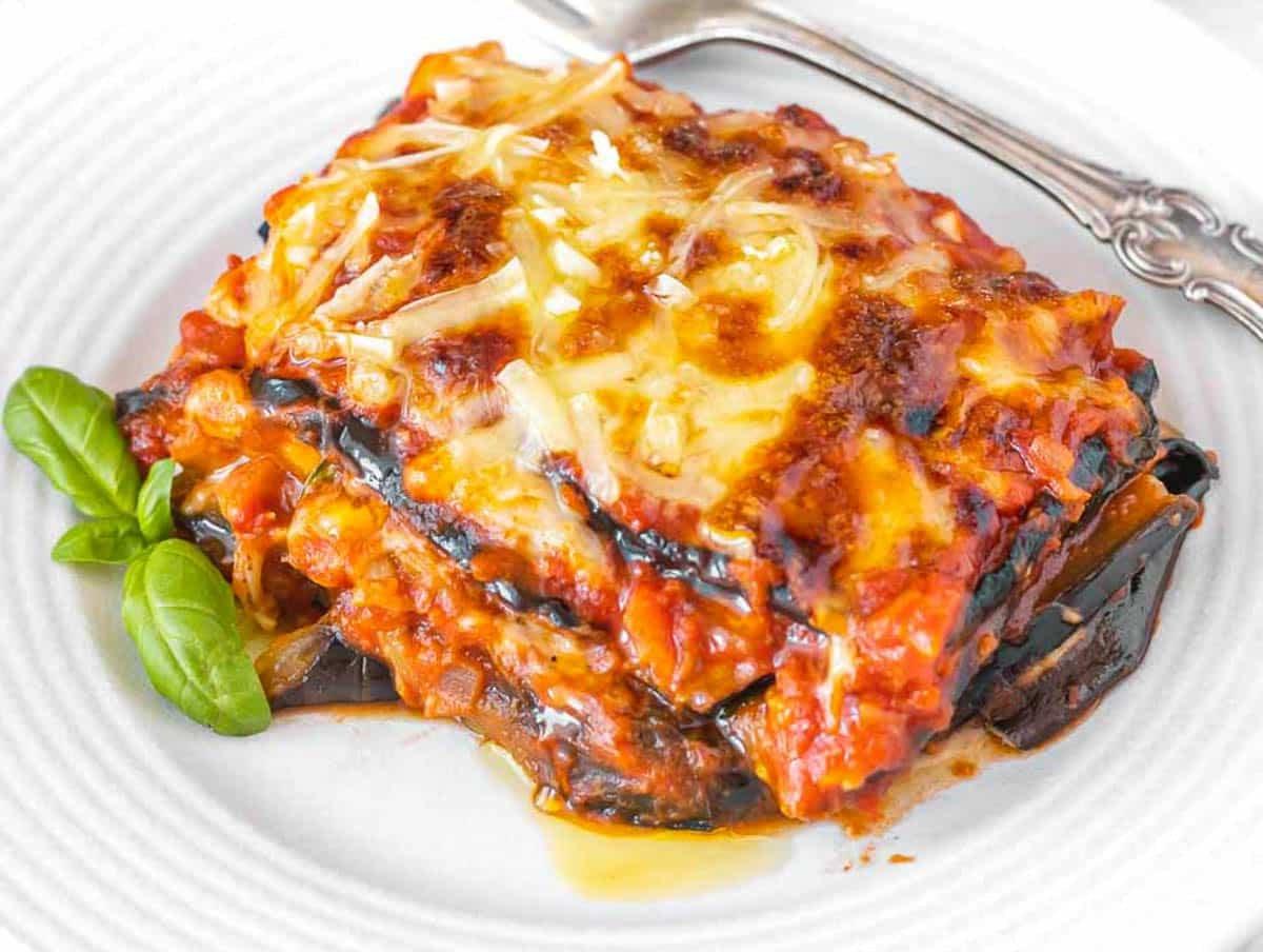 Auberginen-Parmigiana auf einem weißen Teller mit einer silbernen Gabel