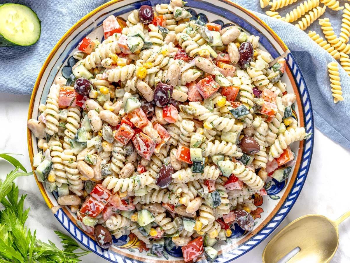 Cremiger Nudelsalat auf einem blauen Teller mit Gurke daneben.