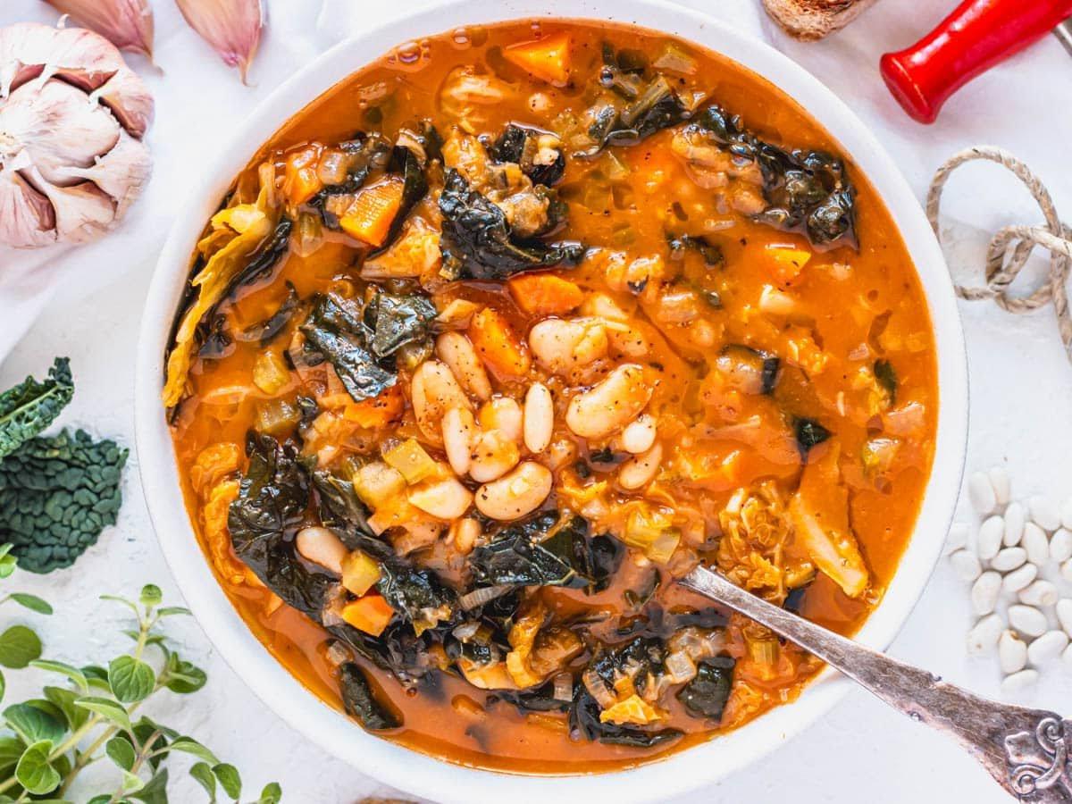 Toskanische weiße Bohnensuppe mit silbernem Löffel und frischen Kräutern daneben