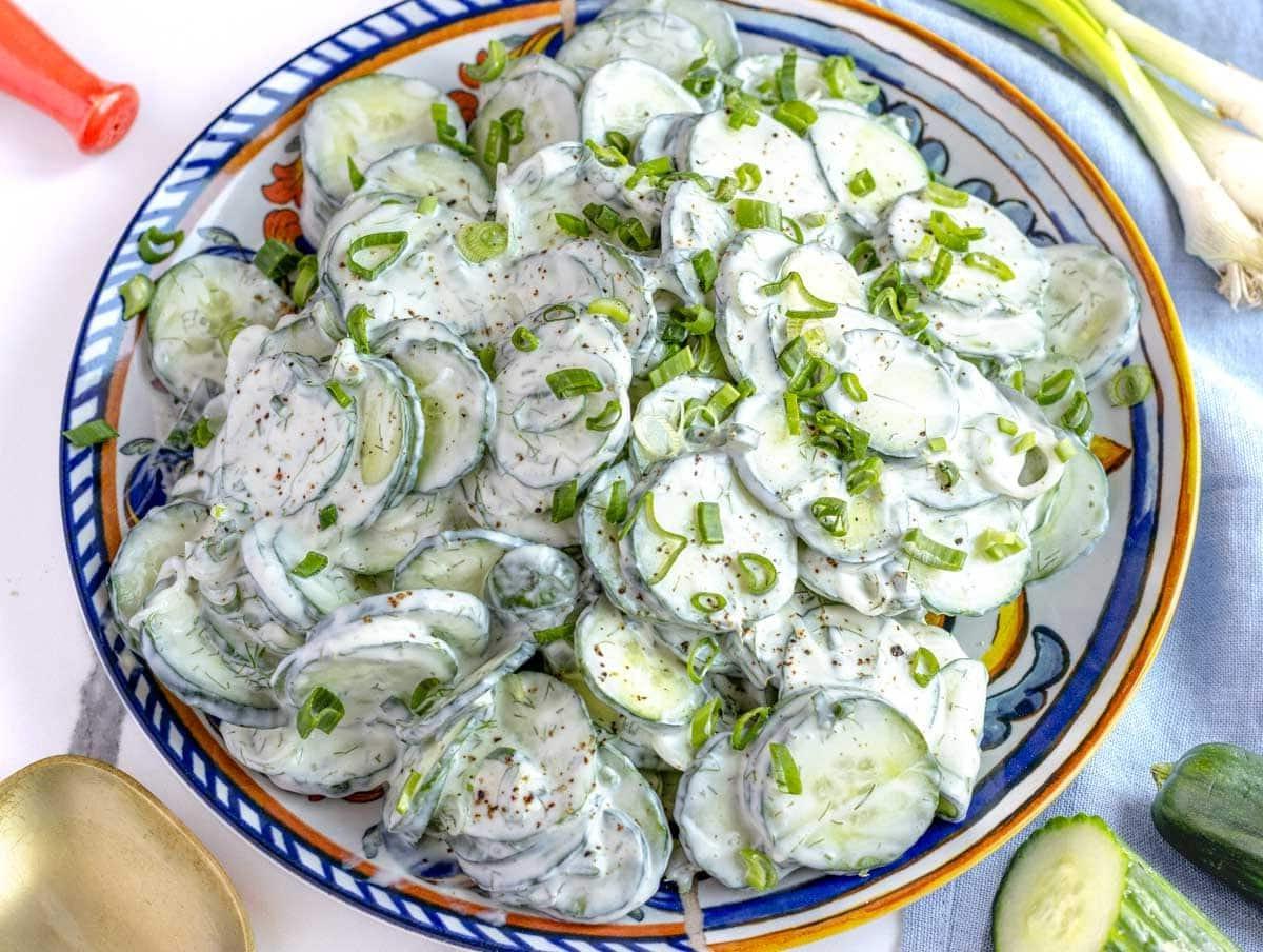 Cremiger Gurkensalat auf einem Teller mit Frühlingszwiebeln daneben
