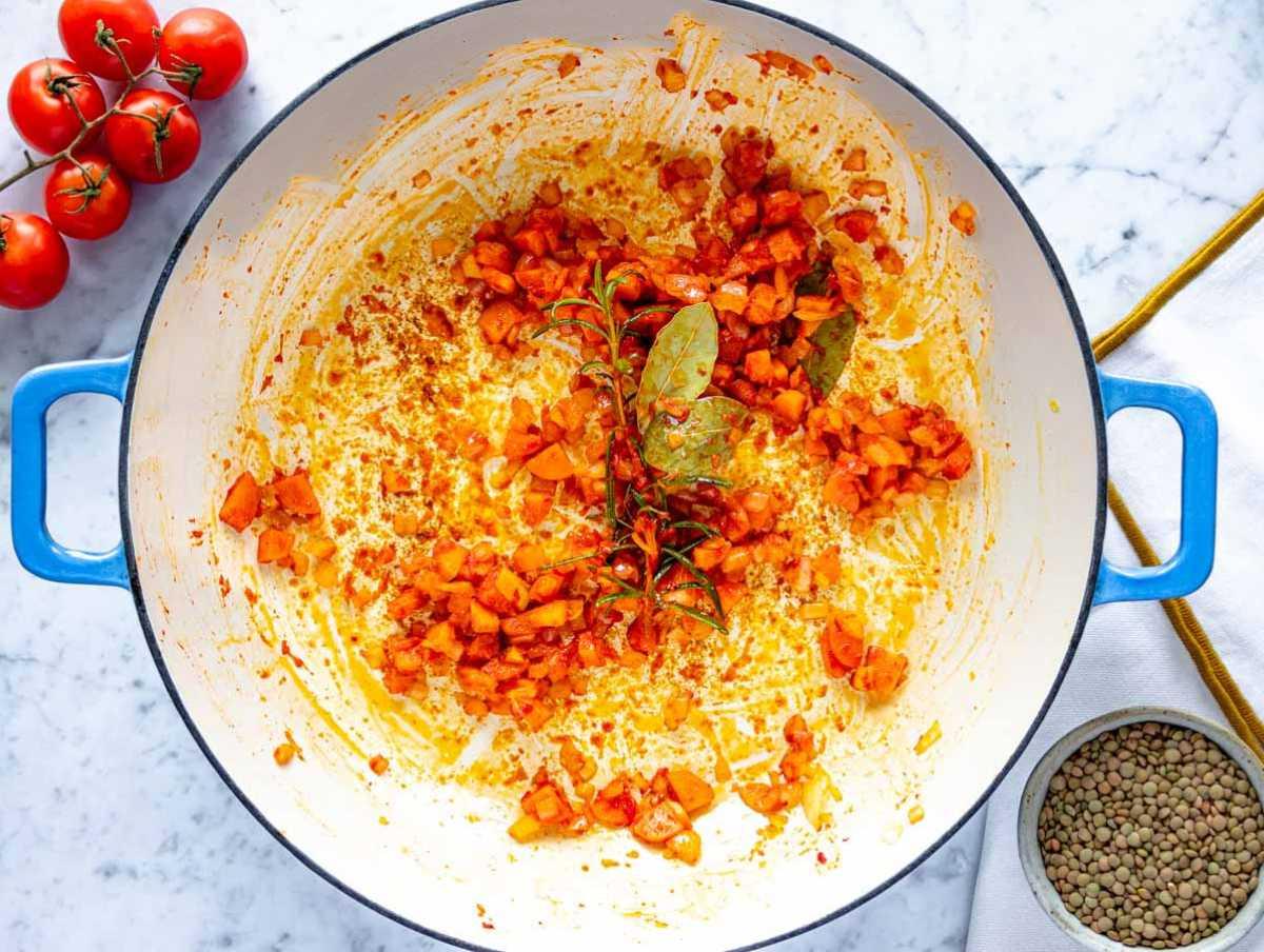 Geschmacksbasis mit Zwiebel, Karotte und Tomatenmark in einer Pfanne anbraten.