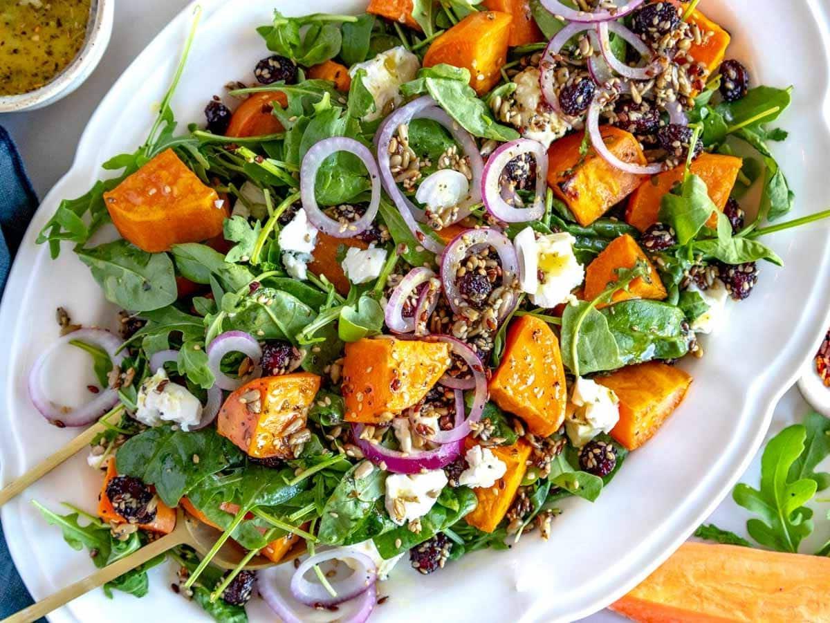 Anleitung zum Anrichten eines Süßkartoffel-Salats auf einem Bett aus Blattsalat.