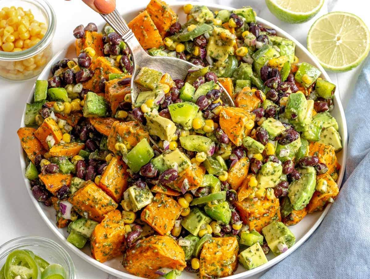 black bean salad with avocado, corn, and a hand holding a spoon