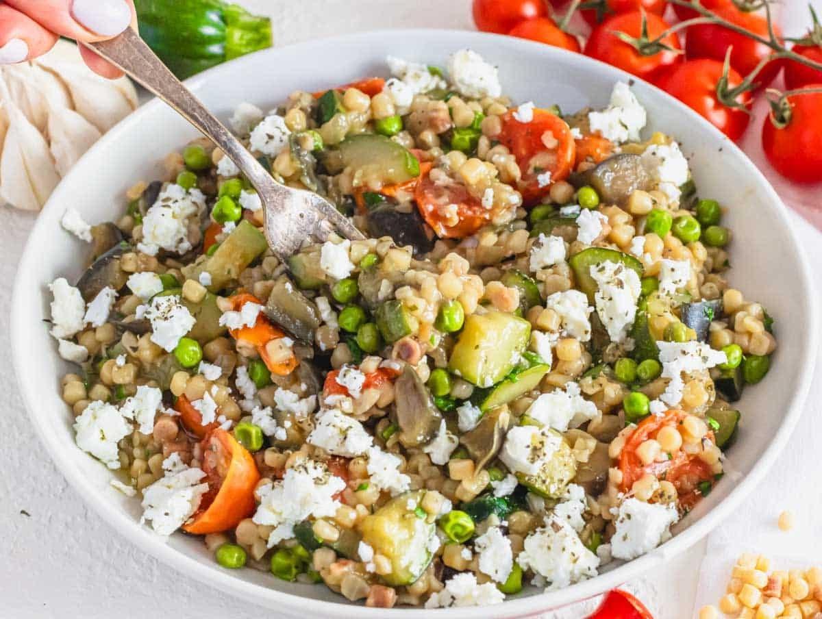 Cremige Fregola in einer Schüssel mit einer Hand.