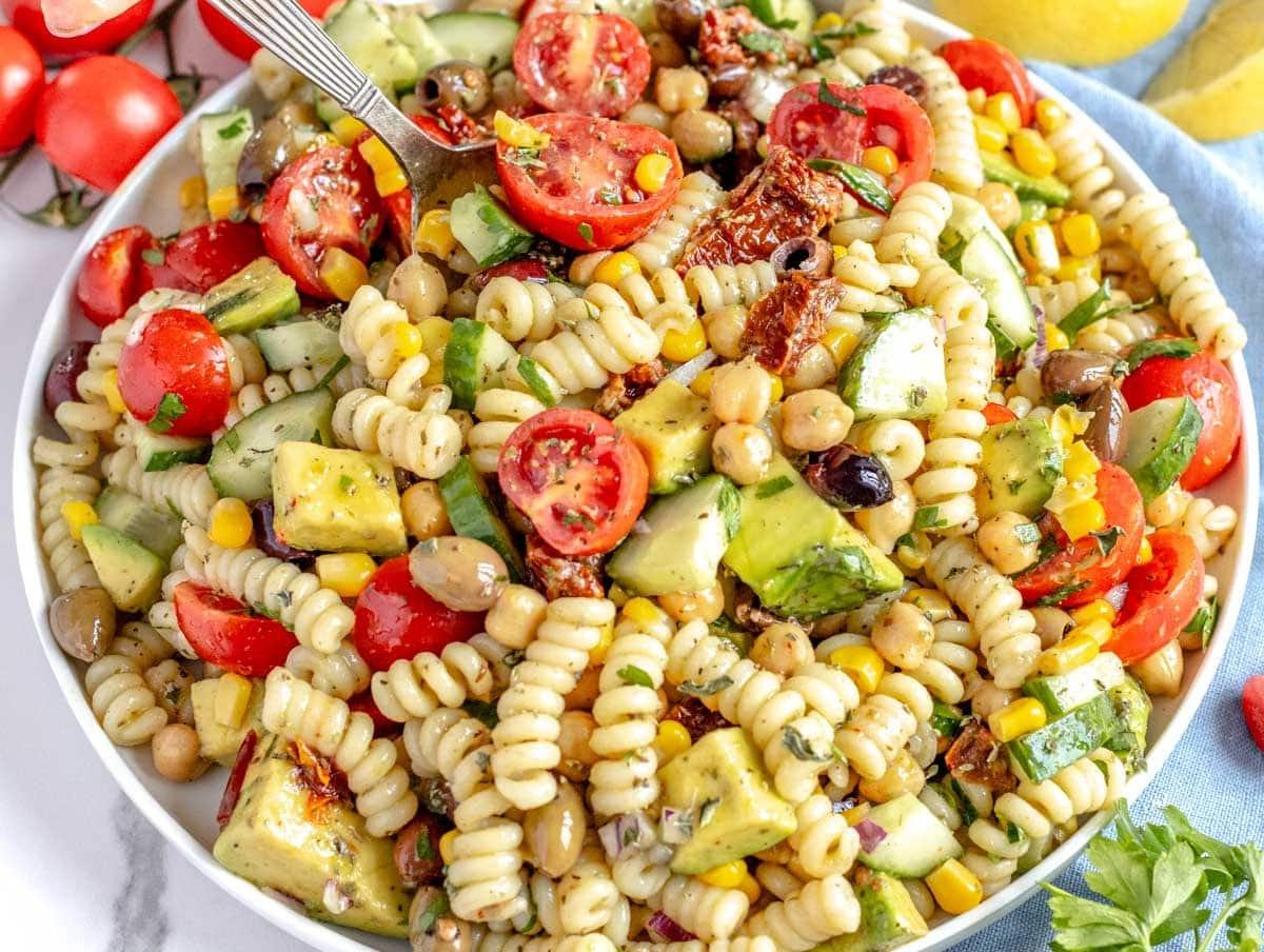 Kichererbsen-Nudelsalat auf einem weißen Teller mit einem Löffel serviert.