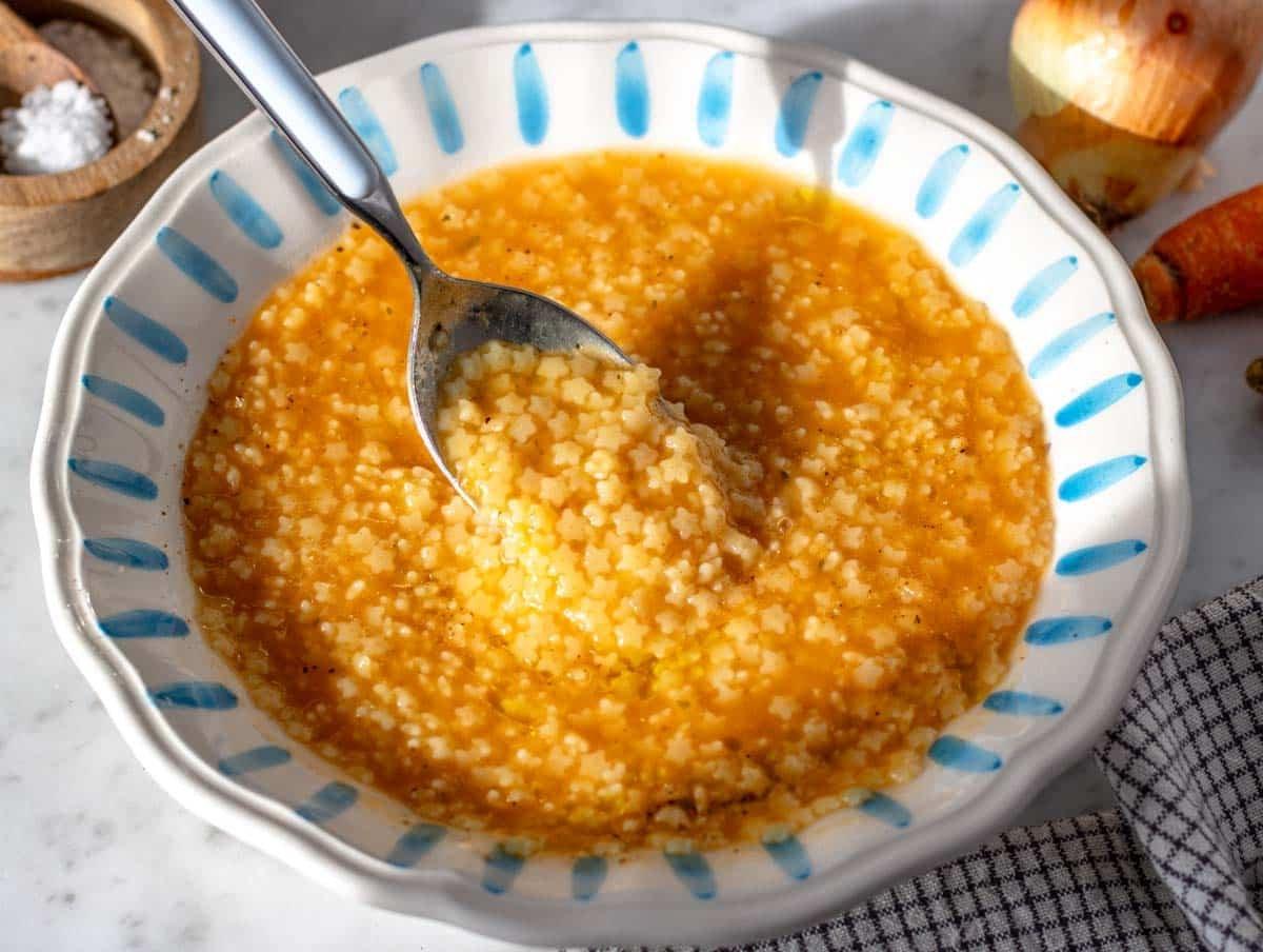 Pastina mit einem blauen Löffel in einer weiß-blauen Schüssel.