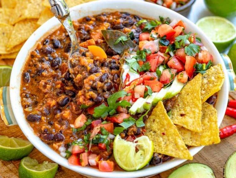 Schwarze Bohnensuppe garniert mit Tortilla, Pico de Gallo, Avocado, Sauerrahm, Koriander und Limettensaft.
