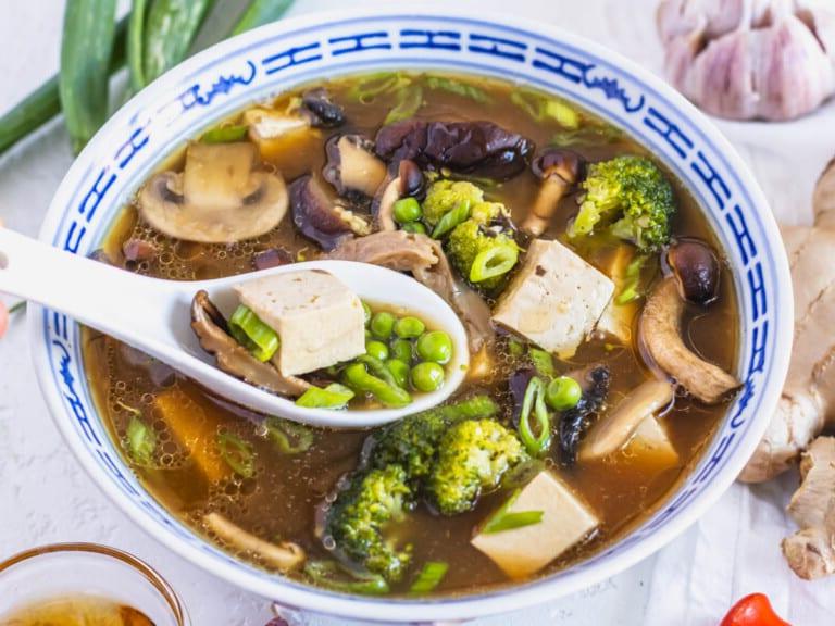 Tofusuppe mit Erbsen, Brokkoli und einem weißen Löffel